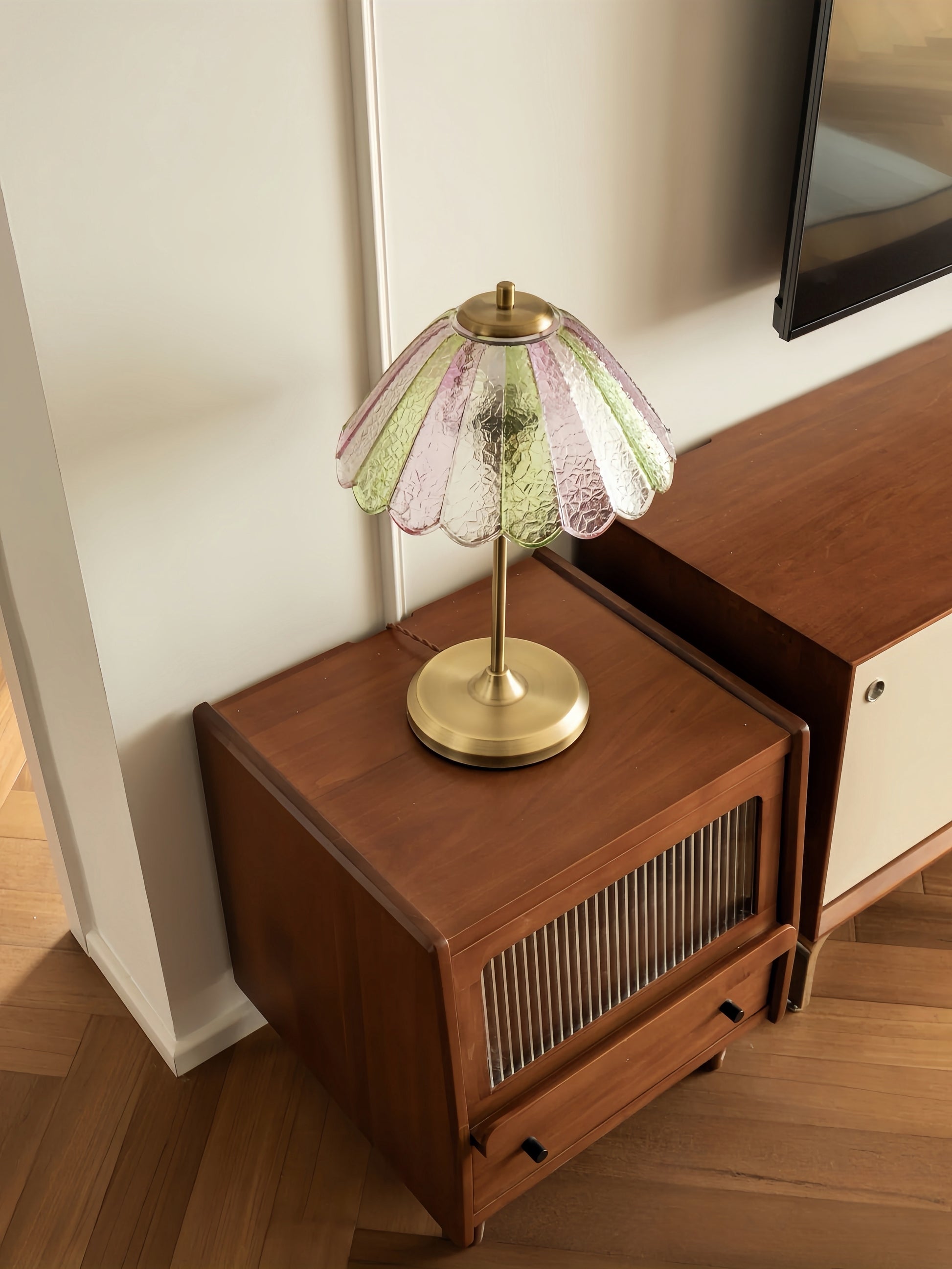 Colorful table lamp with a decorative glass shade on a wooden cabinet.