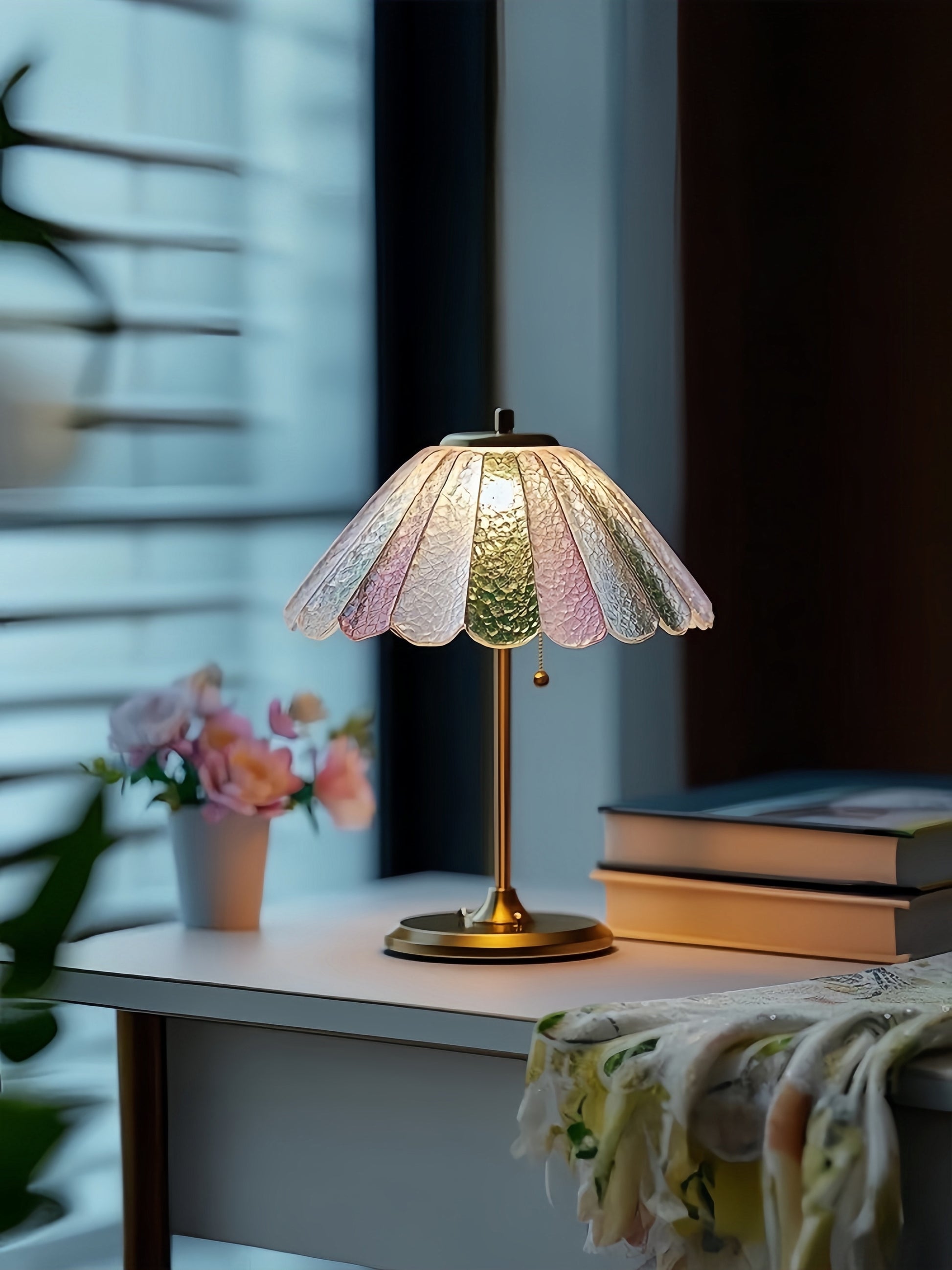 Decorative colorful table lamp with a colorful shade on a table next to books and flowers.