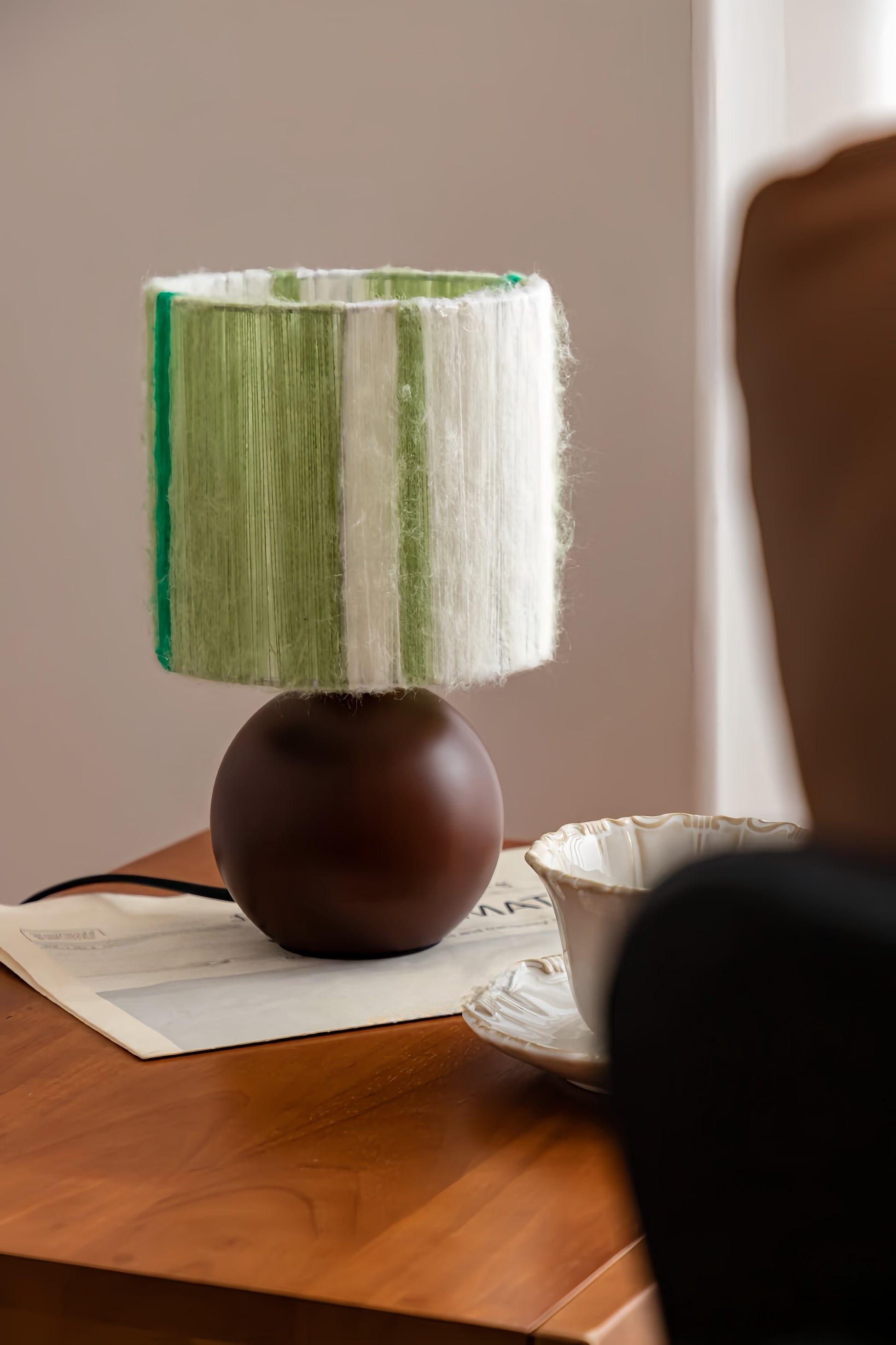 artisan table lamp with a green and white striped shade on a wooden surface.