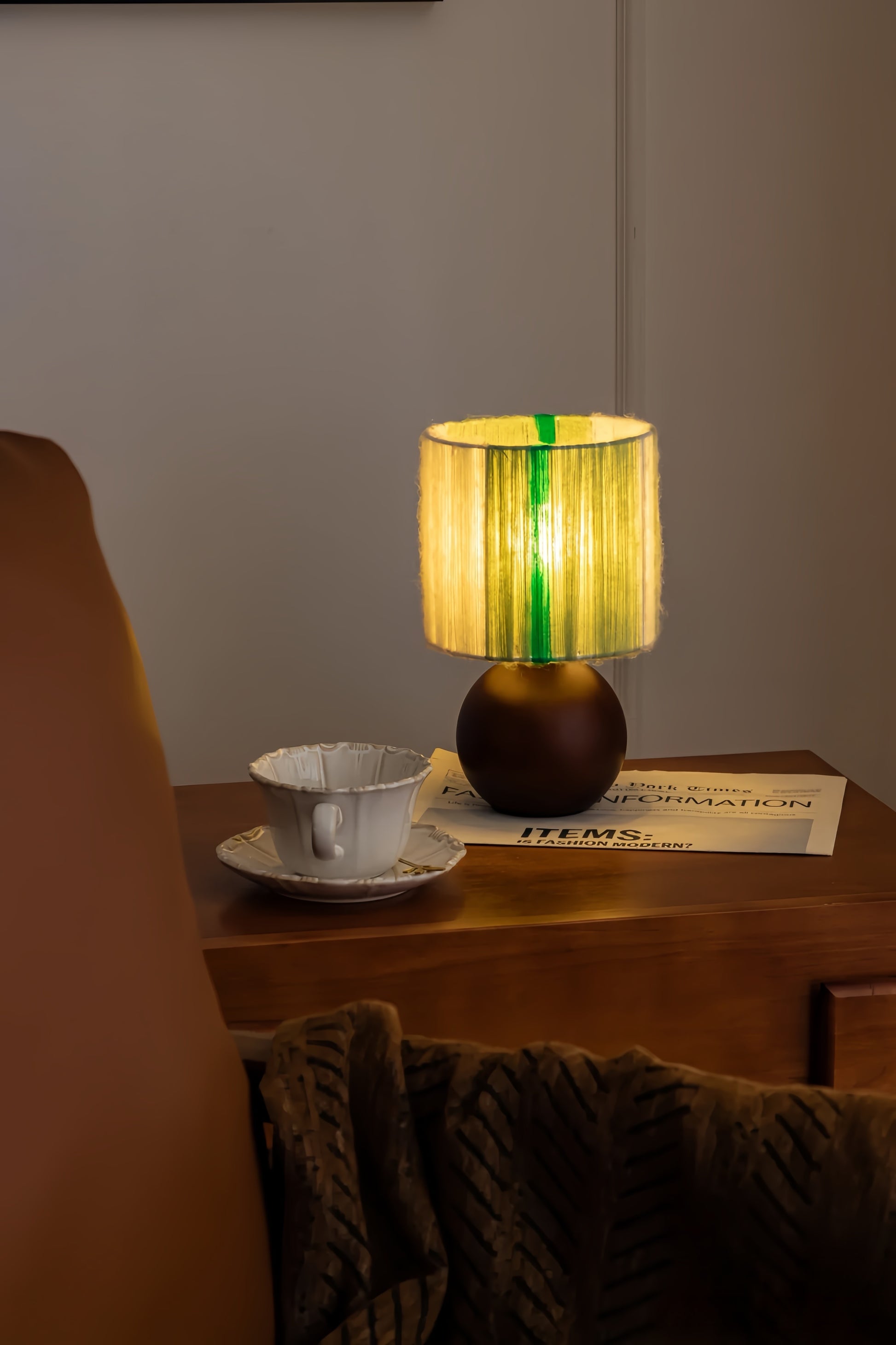 Artisan mohair table lamp with a green and yellow shade on a wooden surface next to a cup and saucer.