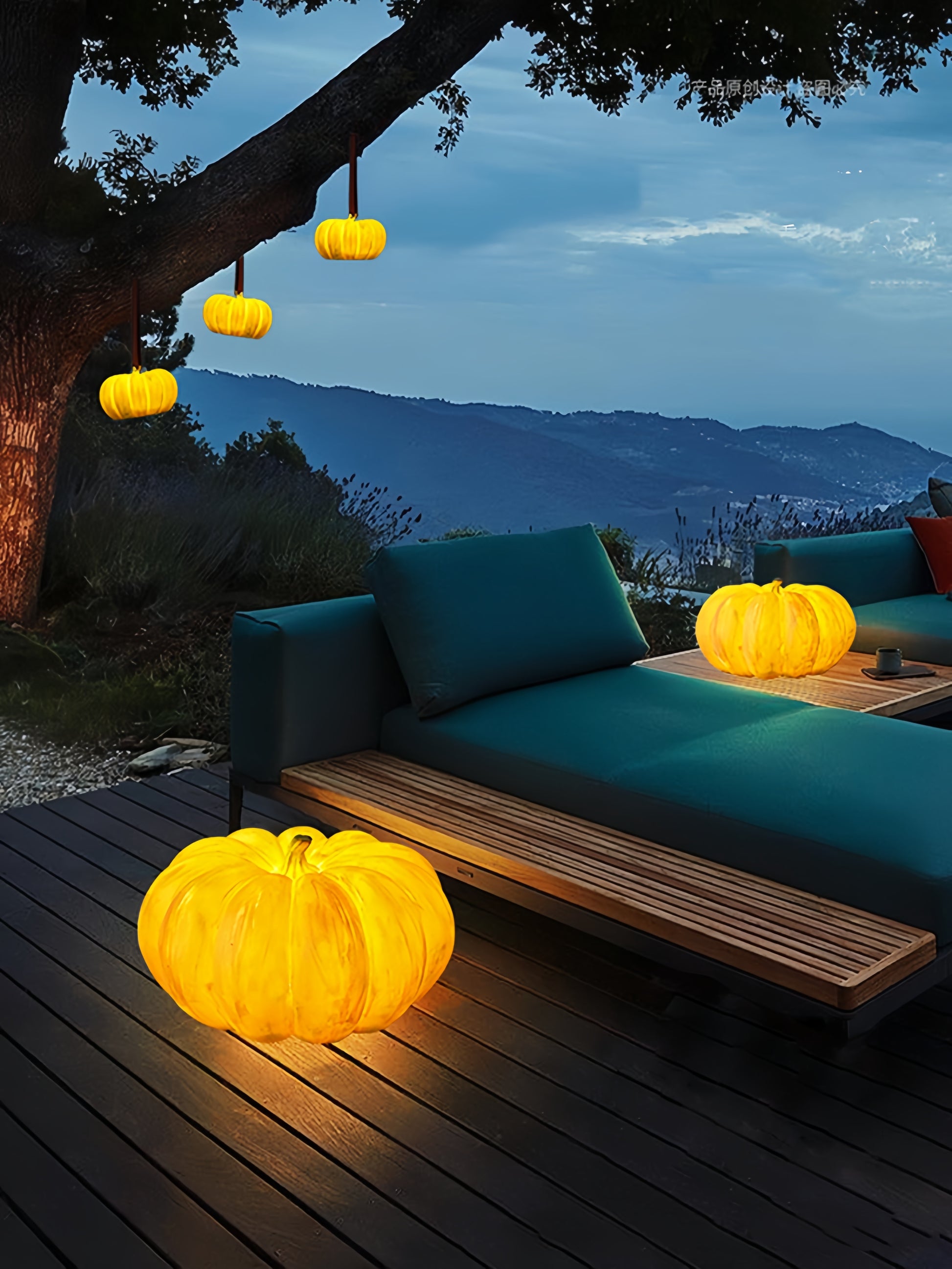 Outdoor evening setting with teal sofa, glowing yellow pumpkin lamp, and mountain view.