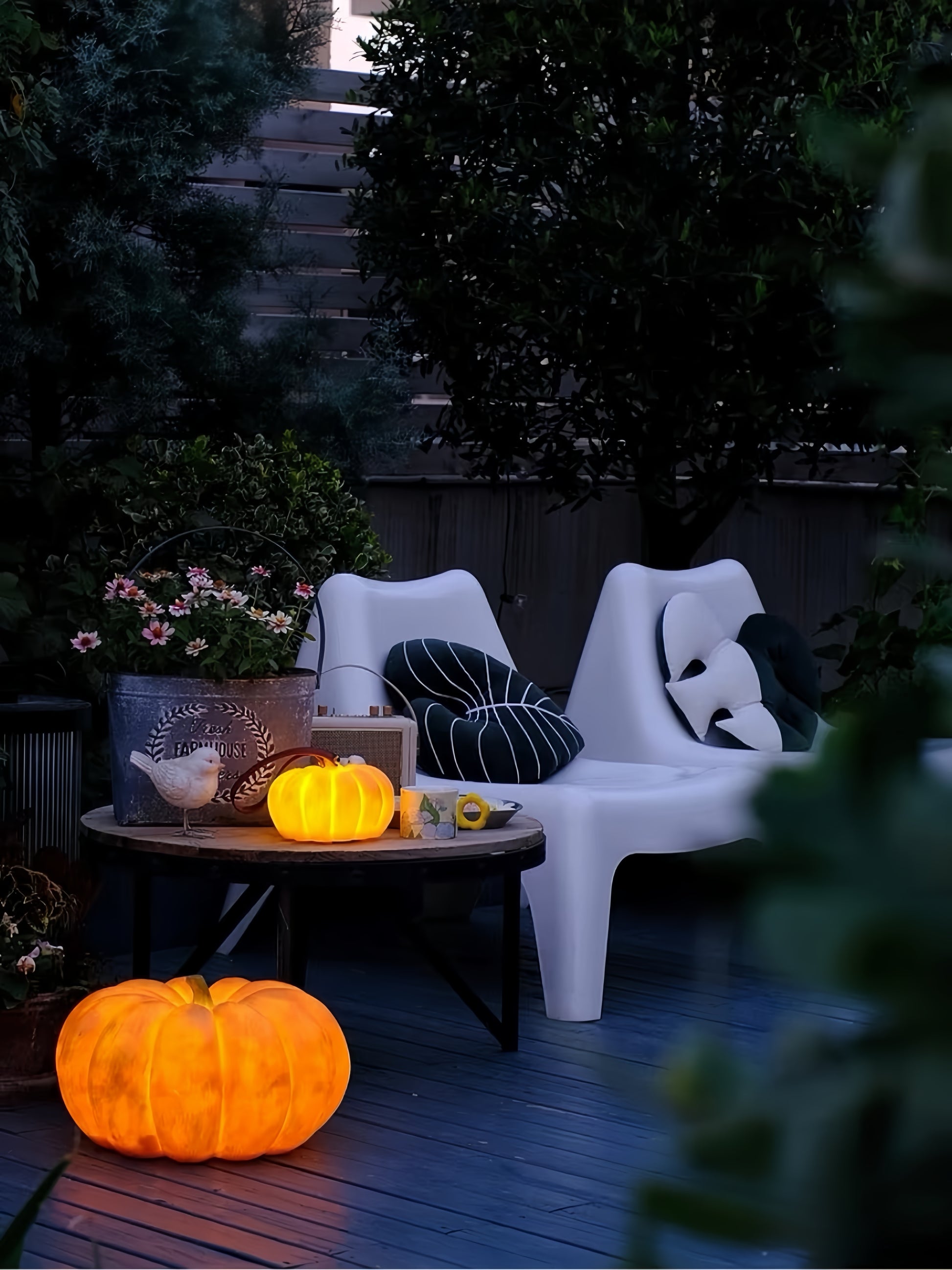 Outdoor setting with white chairs, pumpkin lamps, and decorative items on a wooden deck.