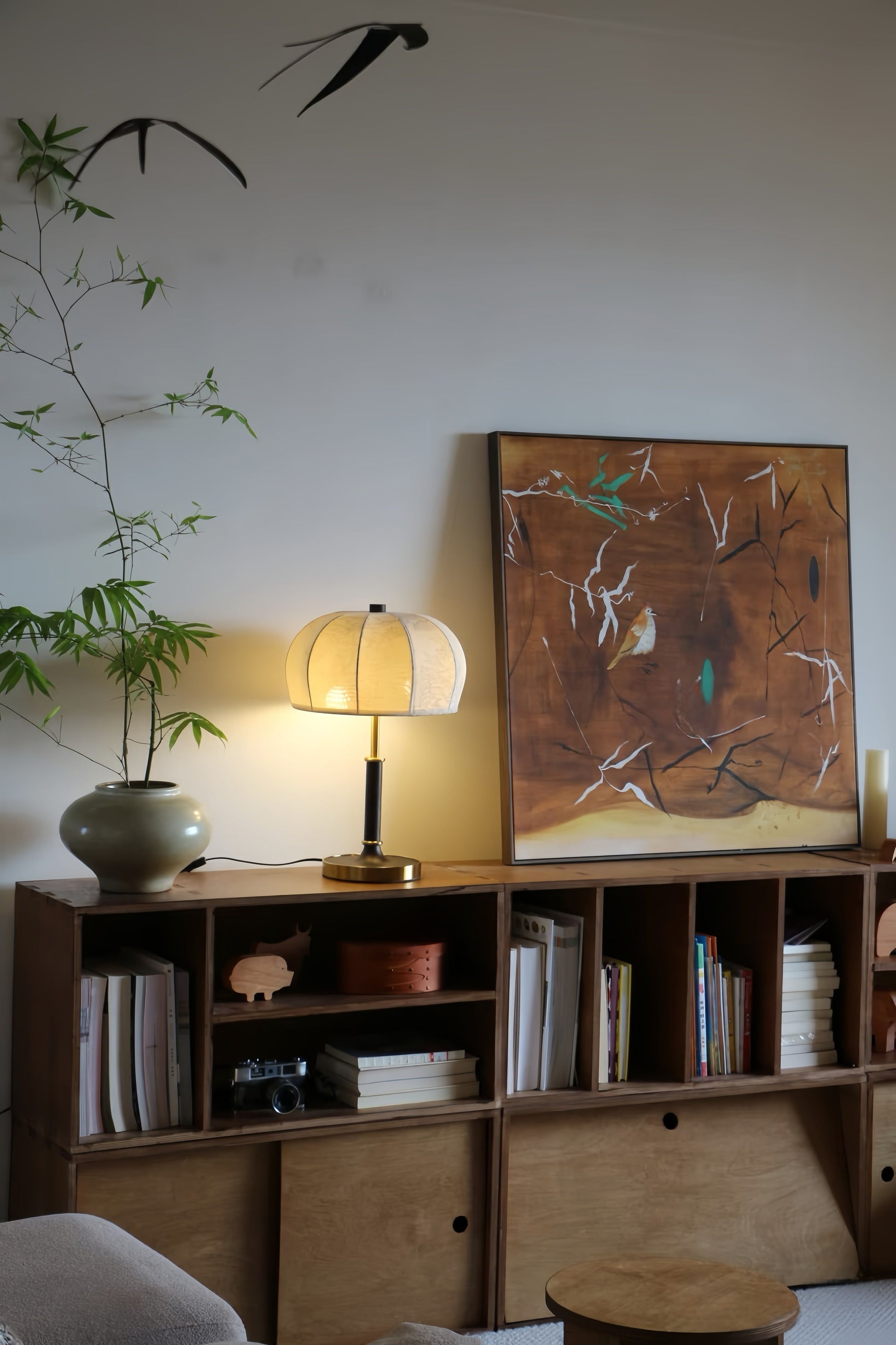 Wooden bookshelf with books, a french vintage table lamp, and a painting in a room setting.