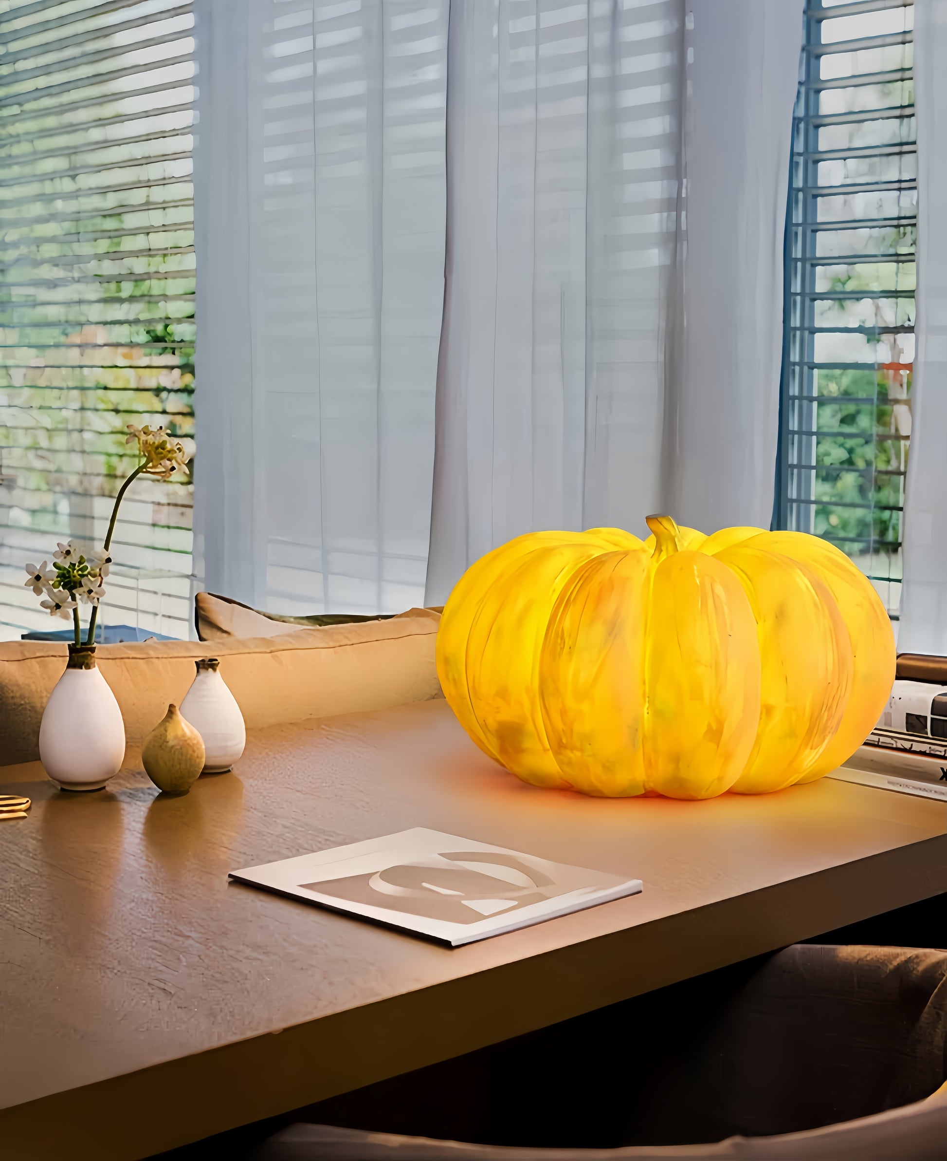 Yellow glass pumpkin lamp on a wooden surface with decorative vases and a magazine in the background.